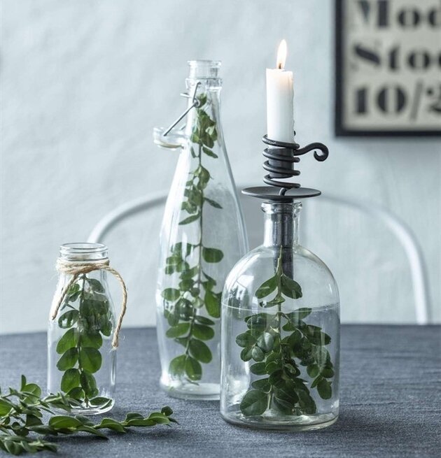 Foto av stilfulla glasflaskor med ljus och gröna blad