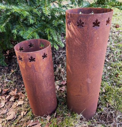 Foto av två cylindriska ljushållare i trädgårdsmiljö