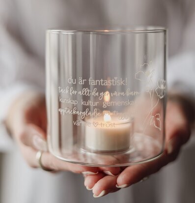 Bild av ljuslykta med graverad text och blomstermotiv i glas