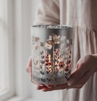 Bild på hand som håller dekorativ glaslykta med floralt motiv