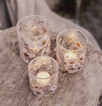 Bild av tre ljuslyktor med blomstermotiv på rustikt träbord