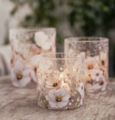 Bild på cylinderformade ljuslyktor i sprucket glas med blommor