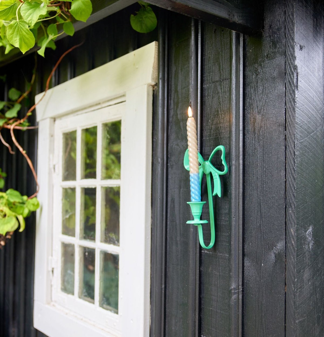 Bild: Utomhus ljusstake i rosett-design på svart träfasad