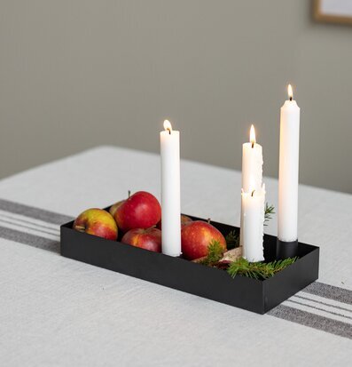 Bild av svart ljusstake med äpplen och grankvistar på duk