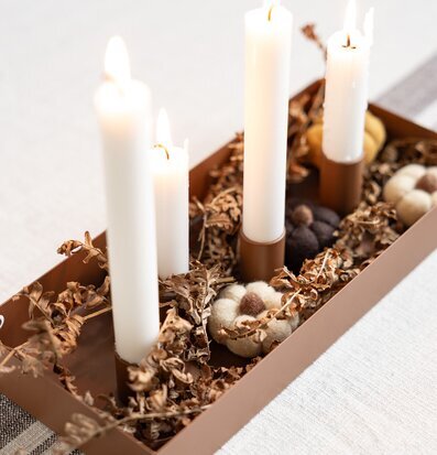 Bild av brun ljusstake med naturmaterial och tända ljus