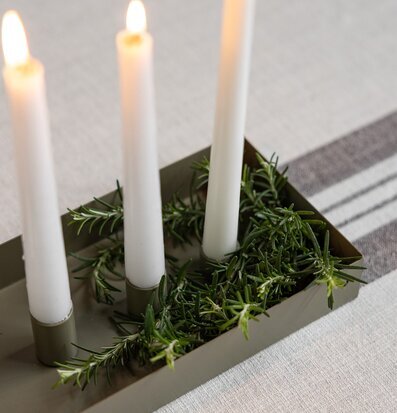 Bild på grön rektangulär ljusstake med vita ljus och rosmarin